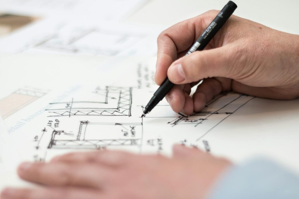 Gros plan d'une main dessinant au stylo des dessins techniques complexes sur un plan, idéal pour les thèmes de l'ingénierie ou de l'architecture.